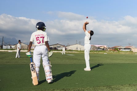 A tall African girl in cricketers' clothing catches a ball as smaller children in pads stand nearby