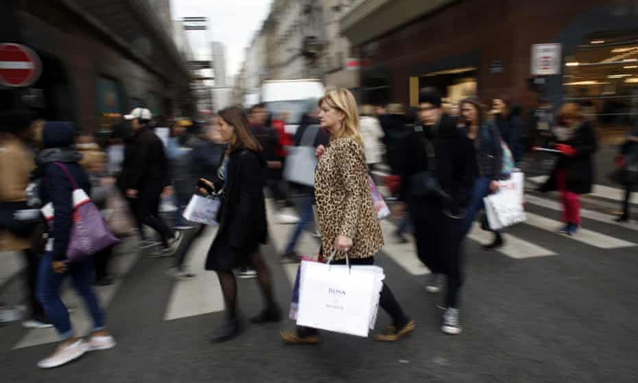 Crowds on pedestrian crossing, one woman in focus carrying Boss shopping bag