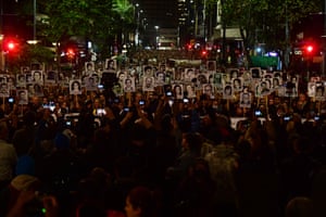A crowd of demonstrators hold up black and white headshots in a nighttime protest