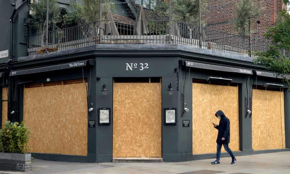 A man with a face mask passes a boarded-up bar in Clapham, south London.