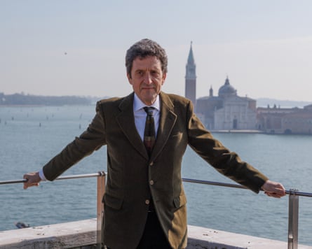 Pietrangelo Buttafuoco, wearing a sage green suit, stands on a balcony overlooking the Venetian lagoon