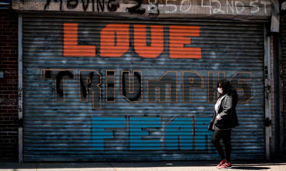 A woman wearing a facemask walks past a shuttered shop reading “love triumphs fear” amid the coronavirus pandemic in Queens, New York City