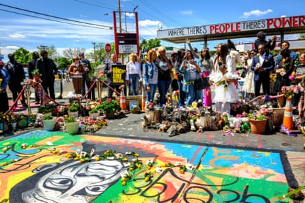 Community members and Floyd family members gather around a mural of George Floyd at George Floyd Square to leave yellow roses and photos in his memory in Minneapolis, Minnesota on Friday, during a tribute marking nearly five years since Floyd’s killing by police. The former gas station is now a community memorial site.