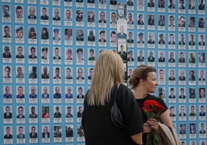 Two women stand in front of a wall of portrait photographs