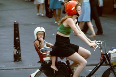 a girl in a cycle helmet pedals with a very young child, also in a helmet in a pillion seat behind her