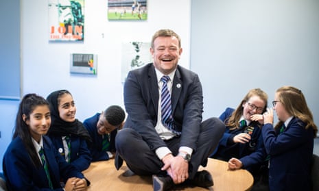 Head James Haseldine sitting on a table surrounded by pupils