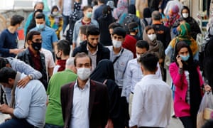 Iranians wearing face masks walk through a market in Tehran, Iran