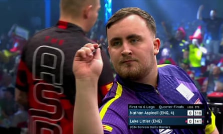 Luke Littler throwing a dart in the foreground with Nathan Aspinall behind him with his back turned to the camera. 