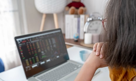 Woman sits at desk while looking at online trading screen on laptop