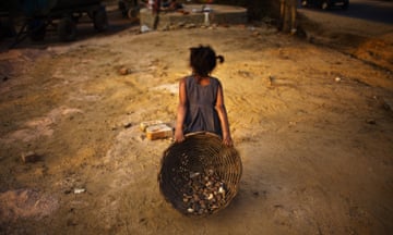 a child dragging a basket of stones at a construction site in India