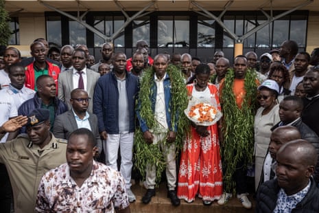 Sabastian Sawe wearing a large green garland stands at the centre of a crowd posing for a photo