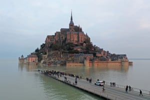 People look at the monastery from the partially submerged road at Mont-Saint-Michel in France
