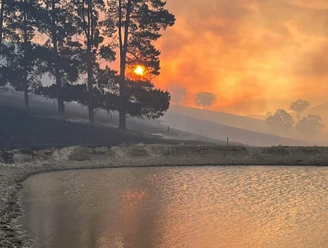 Sun seen through a haze of orange smoke above a water pond