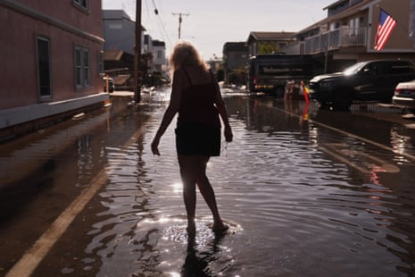 A resident wades barefoot through floodwaters in Huntington Beach, holding her glasses