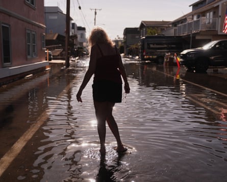 A woman walks through flood water in a street in Huntington Beach, California.