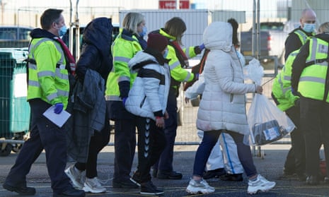 Staff in hi-vis jackets escort young people carrying belongings in plastic bags