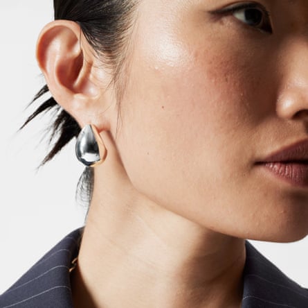 A model with her hair tied back shows her chunky teardrop earrings to the camera
