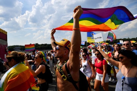 A topless man holding up a Pride flag.