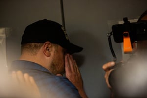 a man stands against a door with his hand concealing his face
