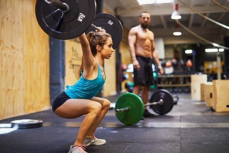 woman lifts weight while man looks at her