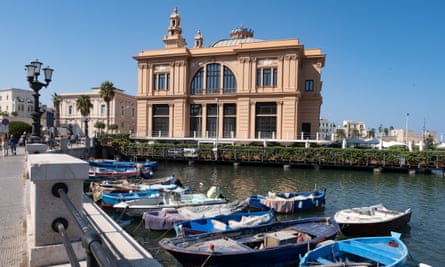 An elegant old building presides over the port, with its little fishing boats, on a sunny day.