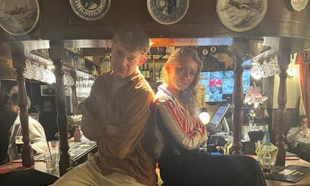 The pair sit at the bar, back to back, with their arms folded.