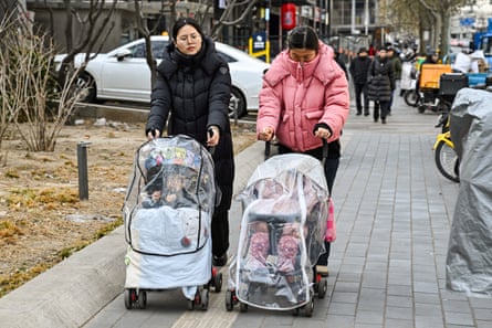 Women in padded jackets push baby strollers along an urban street