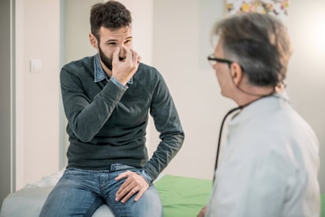 Man holding top of nose and talking to doctor.