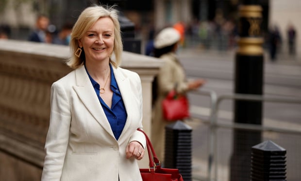 Liz Truss on the street, smiling at someone off camera, in London