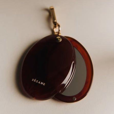 An oval pocket mirror with slide cover. The mirror is tortoise shell with gold Sezane lettering and a gold key chain clasp