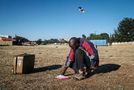 Man crouches to read his bible in a field of dead grass