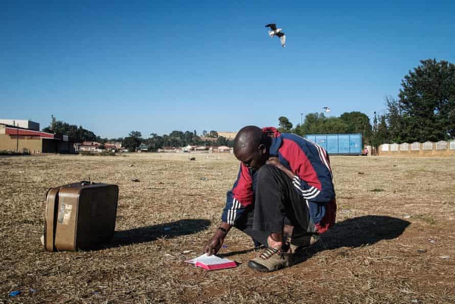 Man bends down to read his Bible in a field of dead grass