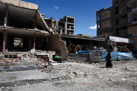 A woman walks past a heavily damaged building.
