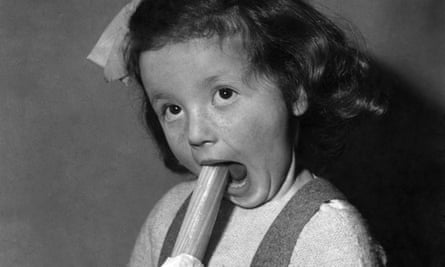 A girl bites a stick of rock in a photo from the 1950s