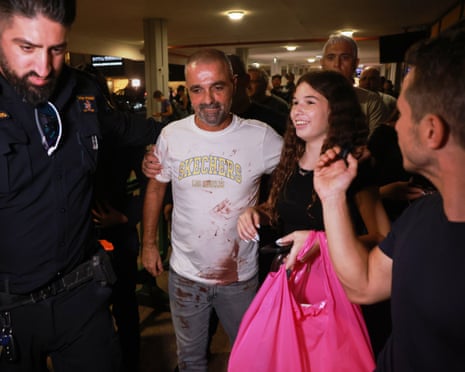 Yaniv Hayoun with blood stains on his shirt walks through a crowd of people at Ben Gurion airport