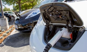 Plug-in electric cars with connectors attached to charging stations in a company car park.