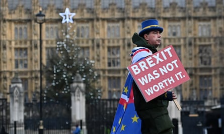 A man wearing an EU flag and holding a sign saying ‘Brexit was not worth it’, with parliament in the background
