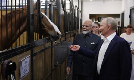 Putin y Modi se encuentran afuera de un establo en un granero; un hermoso caballo castaño con una mancha blanca asoma su cabeza por la puerta.