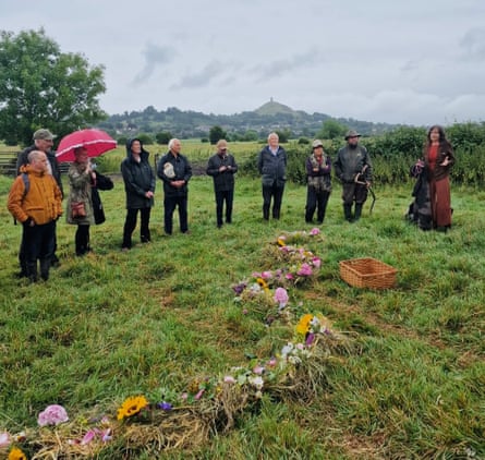 A group of people stand in a field with flowers placed on the floor.