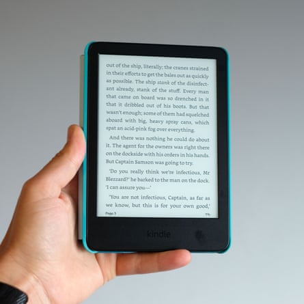 A hand holds up a Kindle e-reader displaying a page of text