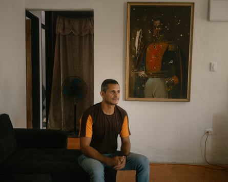 A man sitting in front of a damaged portrait of Símon Bolívar