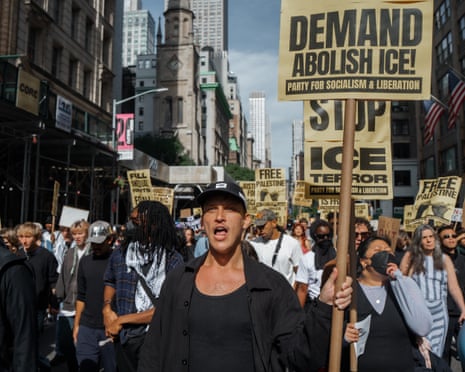A man shouts while marching in an ICE protest, with signs reading 'Abolish ICE' nearby