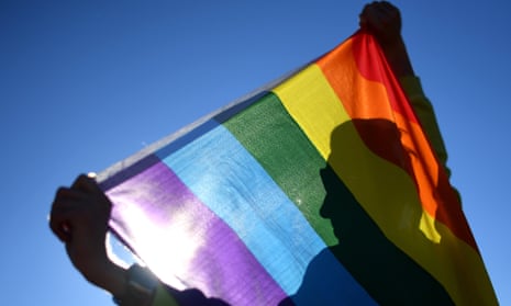 a man in silhouette poses with a rainbow flag