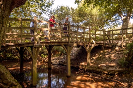 Children play poohsticks on a wooden bridge over a river