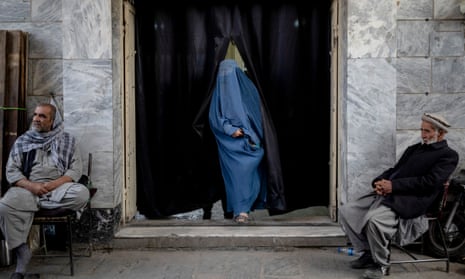 A woman leaves a Shia shrine in a predominantly Hazara neighbourhood while two Taliban men stand guard in Kabul, Afghanistan, November 2021.