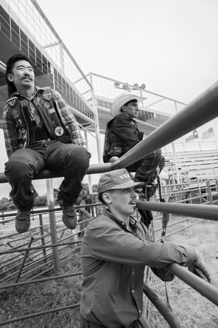 Three men sitting connected aliases opinionated by railings look into a rodeo arena