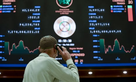 A broker talks on phone as he looks at an index board showing the latest share prices at the Pakistan Stock Exchange in Karachi