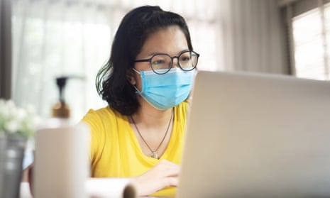 Woman wears a face mask while using a laptop.