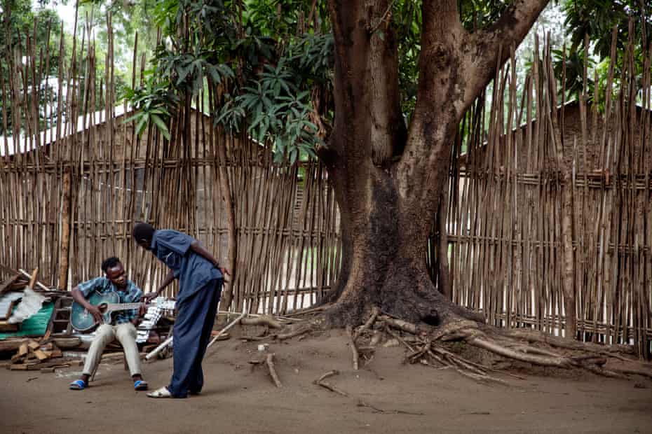 Emmanuel Kembe teaches a young man the guitar