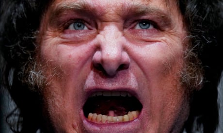 Un primer plano extremo del rostro de un hombre blanco de mediana edad con cabello gris oscuro y salvaje que parece gritar y hablar, con la boca muy abierta y el rostro arrugado.